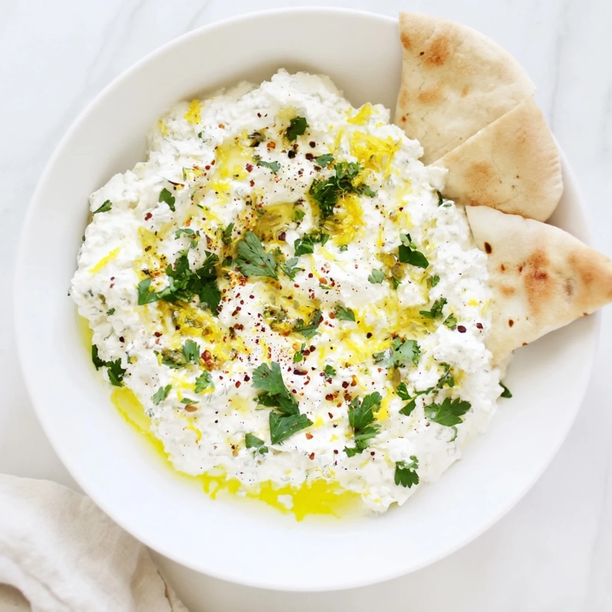 A vibrant close-up of whipped feta, perfectly seasoned with herbs and ready to be scooped up.