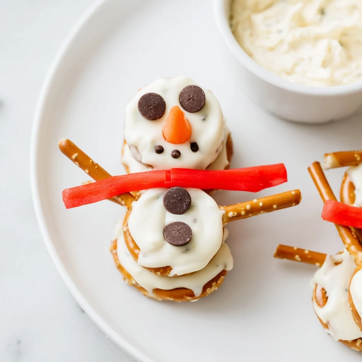 Snowman pretzel and dip platter: whimsical pretzel snowmen with chocolate chip eyes and carrot noses, ready to eat.