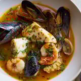 A warm bowl of bouillabaisse, garnished with parsley, ready to be enjoyed with toasted bread and rouille.