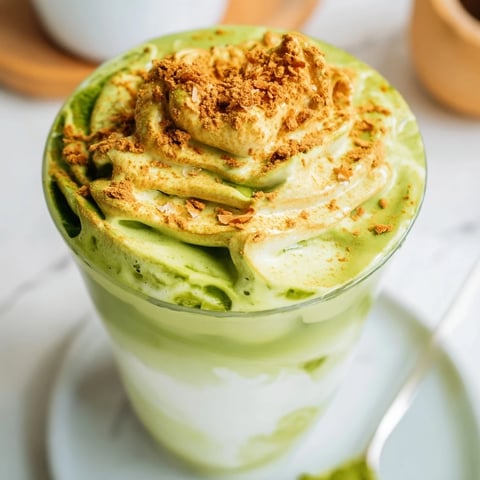 A tall glass of Toasted Coconut Gingerbread Iced Matcha with whipped cream and cinnamon.