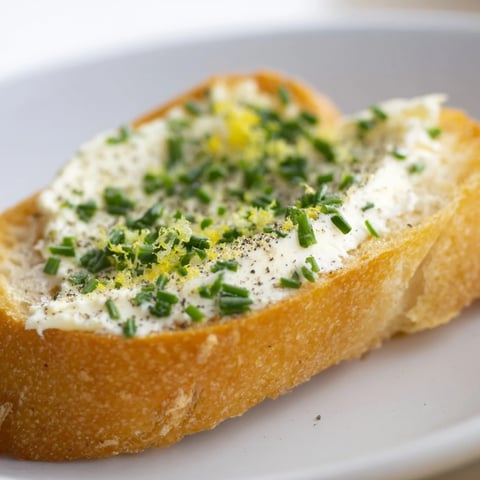 Golden, crispy crostini slices topped with creamy vodka butter spread, garnished with fresh chives and lemon zest on a rustic board.