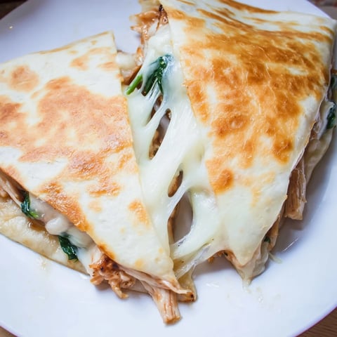A golden-brown Chicken and Spinach Quesadilla sliced into wedges, revealing gooey melted mozzarella and tender fillings on a rustic plate.  