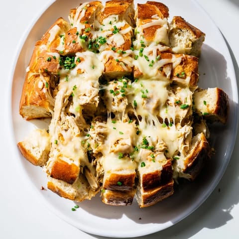 Melted cheese oozes from a Cheesy Leftover Chicken Bake pull-apart bread, a savory, crowd-pleasing dish.