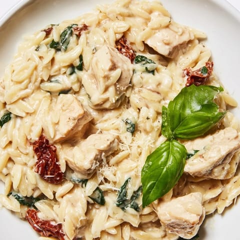 Serving of hot Tuscan Chicken Orzo in a rustic skillet, garnished with grated Parmesan and a sprinkle of red pepper flakes for color.