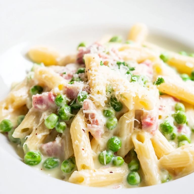 A vibrant skillet of Spring Pea & Ham Pasta featuring bright green peas and golden brown ham chunks in a rich cream sauce.