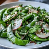 Crisp snap pea and radish salad with fresh mint, parsley, and creamy tahini dressing for a vibrant spring dish.